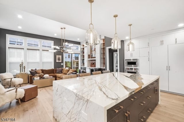 kitchen featuring white cabinetry, light wood-type flooring, recessed lighting, open floor plan, and hanging light fixtures