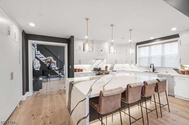 kitchen featuring a sink, dishwasher, white cabinets, light wood-style flooring, and a kitchen island