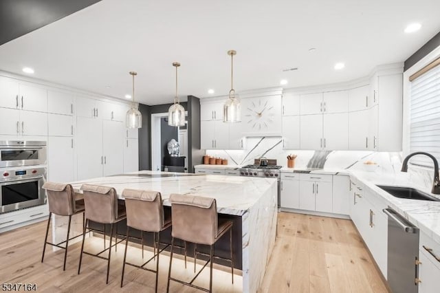 kitchen with a sink, stainless steel appliances, recessed lighting, light wood-style flooring, and wall chimney range hood