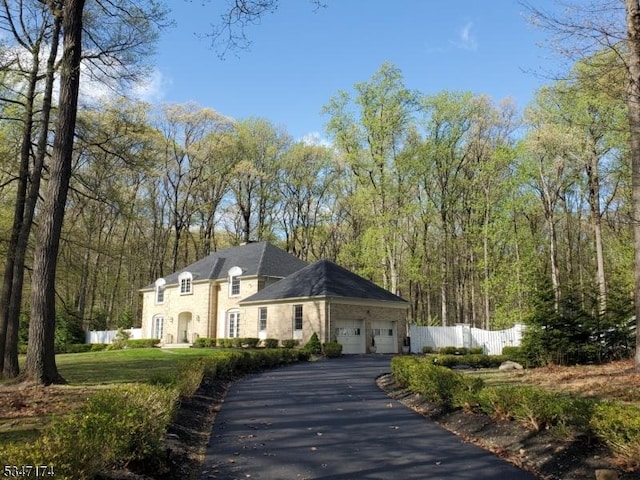 view of front facade featuring a garage, a view of trees, fence, and driveway