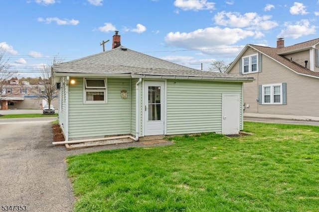 rear view of property with a lawn and roof with shingles