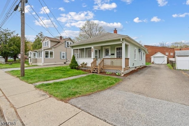bungalow-style home featuring a front lawn, a detached garage, driveway, a chimney, and covered porch