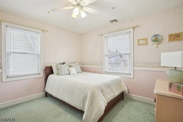 carpeted bedroom featuring baseboards, visible vents, wallpapered walls, and ceiling fan