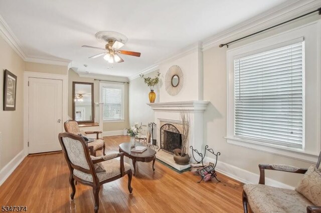 living area featuring a high end fireplace, crown molding, light wood-style flooring, and a ceiling fan