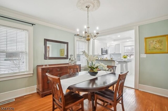 dining area with crown molding, light wood-type flooring, baseboards, visible vents, and an inviting chandelier