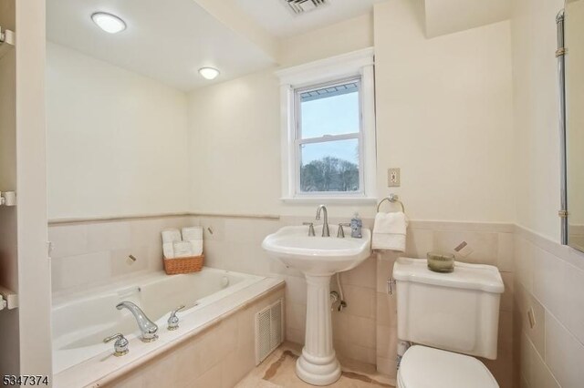 full bath featuring visible vents, toilet, wainscoting, and a garden tub