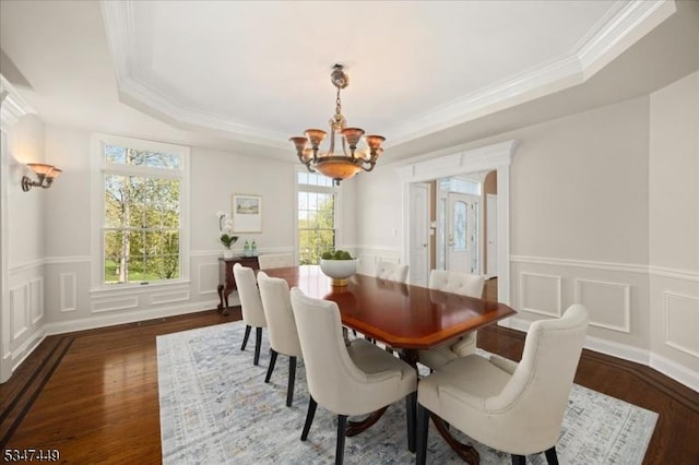 dining space featuring an inviting chandelier, crown molding, a decorative wall, wood finished floors, and a tray ceiling