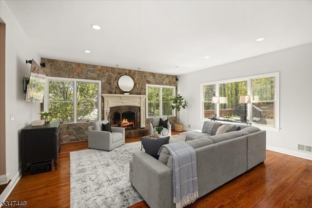 living area with a stone fireplace, visible vents, wood finished floors, baseboards, and recessed lighting