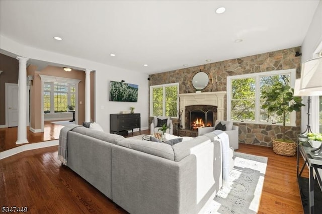living area with a fireplace, decorative columns, wood finished floors, and a wealth of natural light