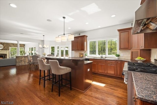 kitchen featuring stainless steel gas stove, dark wood-type flooring, wall chimney exhaust hood, and open floor plan