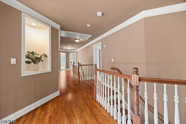 corridor featuring attic access, wood finished floors, baseboards, an upstairs landing, and ornamental molding
