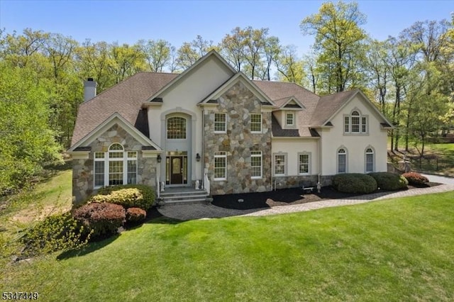 view of front of property featuring a front yard, a chimney, stone siding, and stucco siding