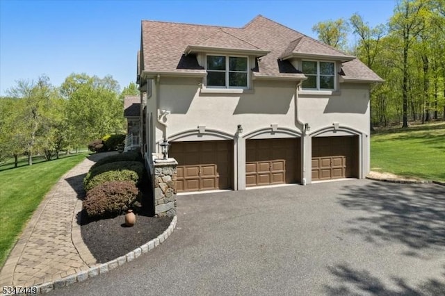 view of property exterior featuring roof with shingles, an attached garage, aphalt driveway, stucco siding, and a yard