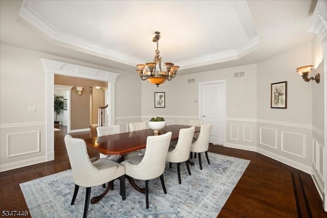 dining area with a tray ceiling, dark wood-style flooring, crown molding, an inviting chandelier, and a decorative wall