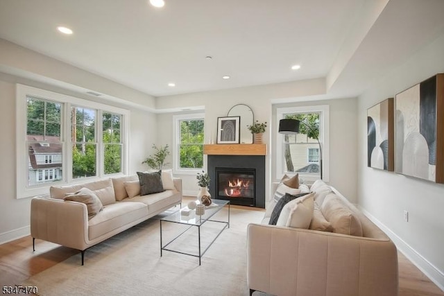 living area featuring a glass covered fireplace, light wood-type flooring, recessed lighting, and baseboards