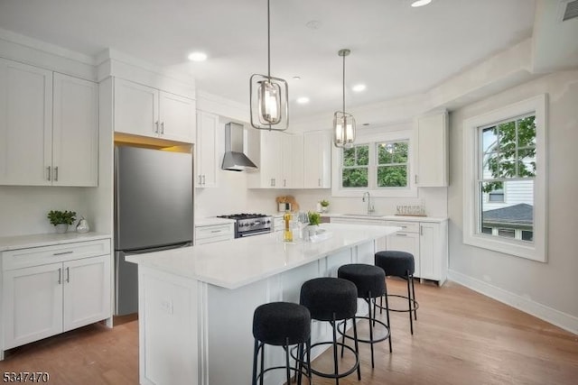 kitchen with light wood-type flooring, stainless steel appliances, a kitchen breakfast bar, and wall chimney range hood