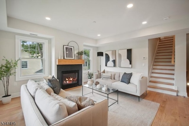 living room with light wood-type flooring, a glass covered fireplace, baseboards, and a healthy amount of sunlight