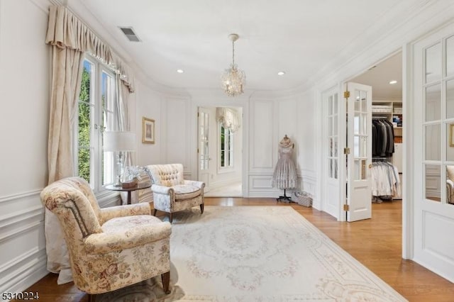 sitting room with a notable chandelier, french doors, visible vents, a decorative wall, and wood finished floors