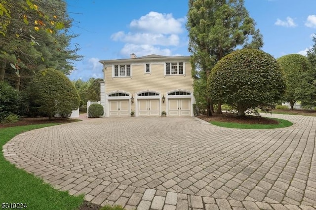 view of front facade with a chimney, an attached garage, and curved driveway