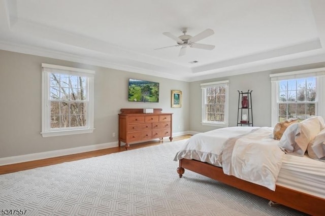 bedroom with wood finished floors, multiple windows, and a raised ceiling