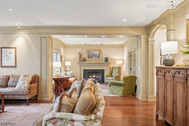 living room with a warm lit fireplace, dark wood-style flooring, crown molding, and decorative columns
