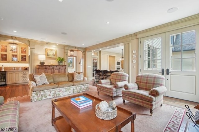 living area with recessed lighting, beverage cooler, light wood finished floors, ornamental molding, and arched walkways