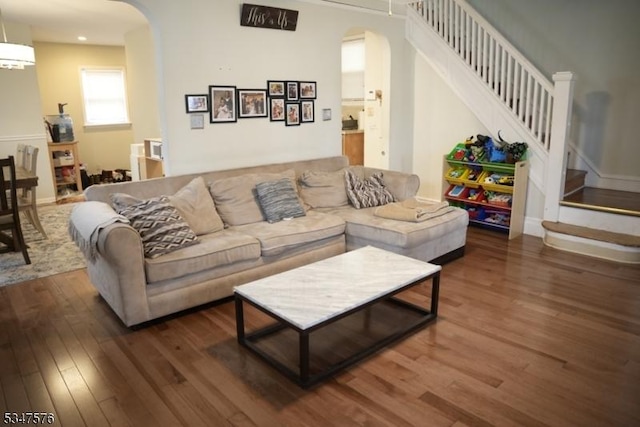 living area with arched walkways, wood finished floors, and stairs