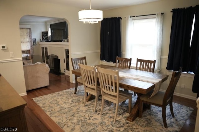 dining area featuring a fireplace, wood finished floors, and arched walkways