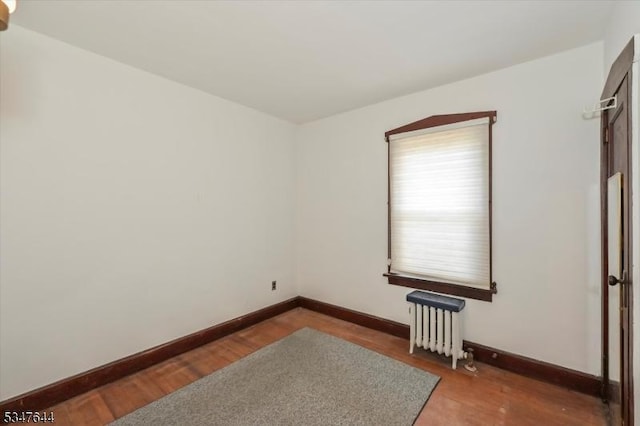 unfurnished room featuring radiator heating unit, baseboards, and wood finished floors
