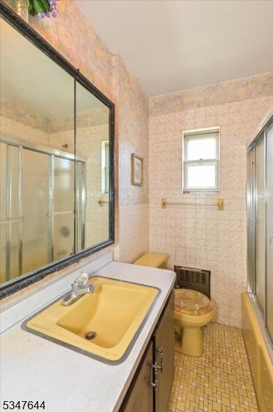 full bathroom with toilet, tile walls, vanity, and enclosed tub / shower combo