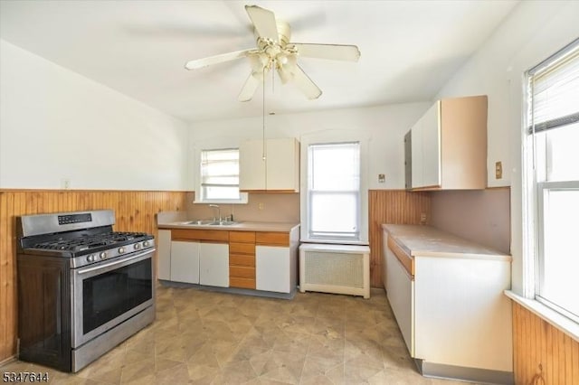 kitchen with stainless steel range with gas cooktop, light countertops, a sink, wood walls, and radiator