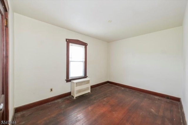 spare room featuring radiator, baseboards, and dark wood finished floors