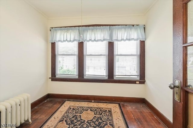 empty room with radiator heating unit, wood finished floors, baseboards, and ornamental molding
