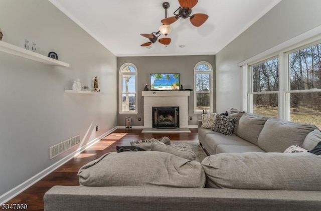 living room with visible vents, a fireplace with raised hearth, ceiling fan, and crown molding