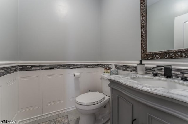 half bath featuring toilet, tile walls, wainscoting, tile patterned flooring, and vanity