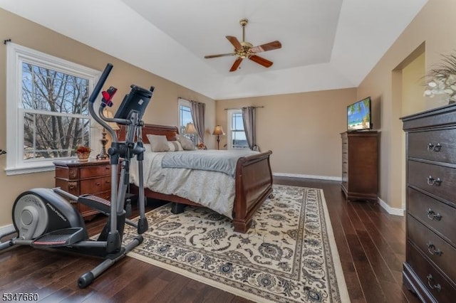 bedroom featuring dark wood-type flooring, a raised ceiling, baseboards, and ceiling fan