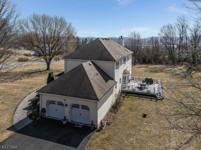 view of side of home with a chimney, aphalt driveway, a shingled roof, a wooden deck, and a garage