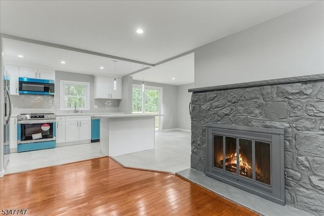7 Mondamin Rd, Vernon Twp, NJ 07422 - kitchen featuring appliances with stainless steel finishes, white cabinetry, light countertops, light wood finished floors, and a stone fireplace