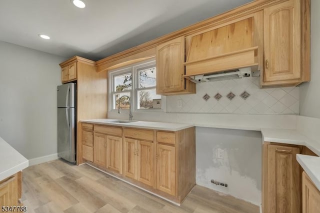 kitchen featuring tasteful backsplash, freestanding refrigerator, a sink, and light wood-type flooring