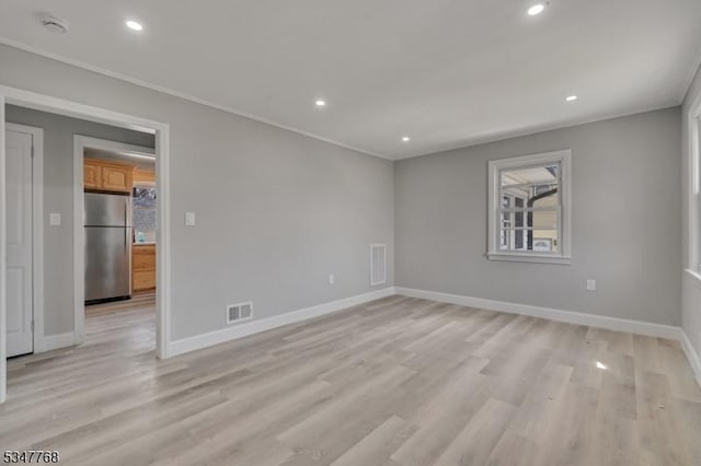 empty room featuring visible vents, baseboards, ornamental molding, and light wood-style flooring