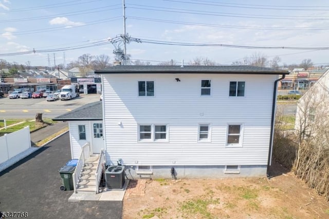 rear view of property featuring central AC, fence, and roof with shingles