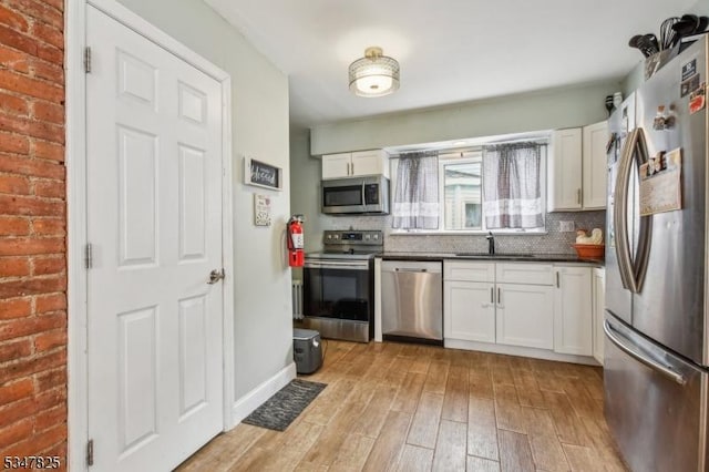 kitchen featuring light wood finished floors, a sink, stainless steel appliances, white cabinetry, and tasteful backsplash