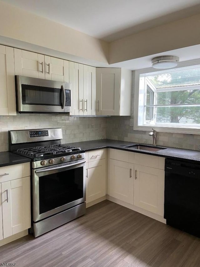kitchen featuring backsplash, appliances with stainless steel finishes, dark countertops, wood finished floors, and a sink