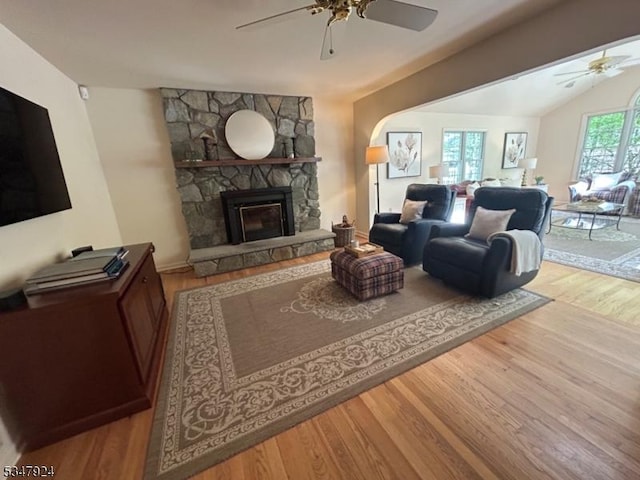 living area featuring a stone fireplace, a ceiling fan, wood finished floors, and lofted ceiling
