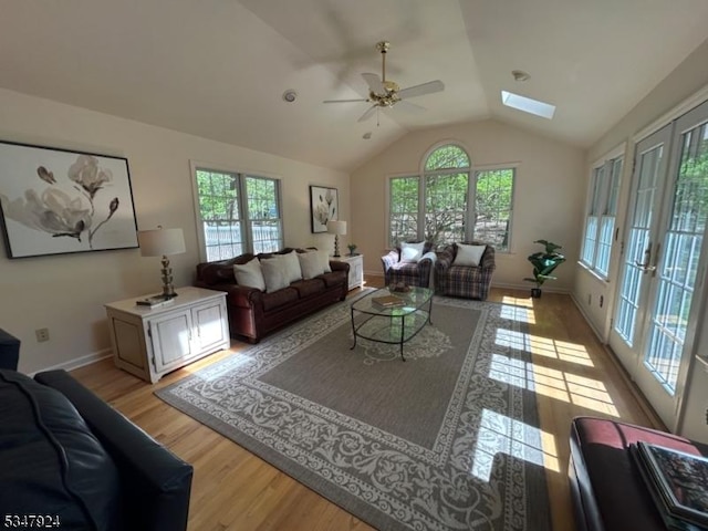 living room with baseboards, a ceiling fan, light wood finished floors, and lofted ceiling with skylight