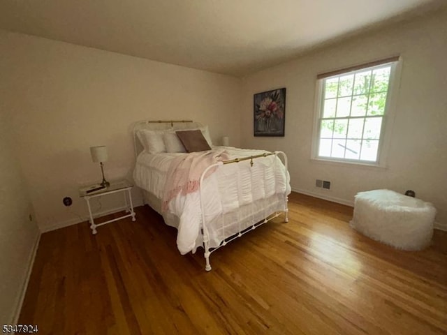 bedroom with baseboards, visible vents, and wood finished floors
