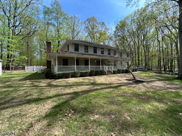 view of front of home featuring fence, covered porch, a chimney, and a front yard