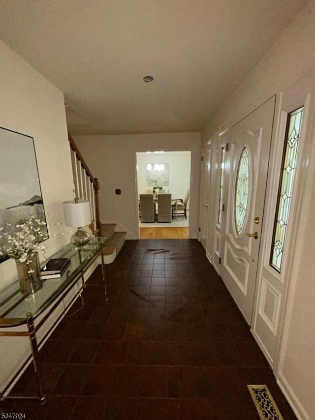 foyer entrance with stairway, dark tile patterned floors, and visible vents