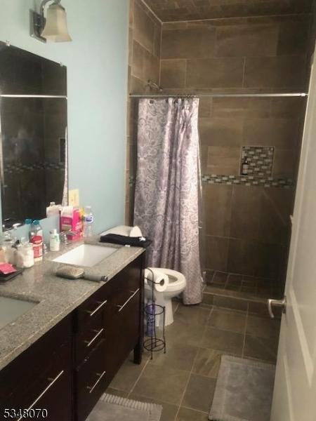 bathroom featuring double vanity, toilet, a shower stall, and a sink