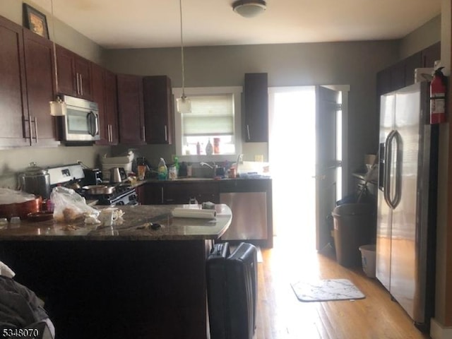 kitchen with a peninsula, light wood-style floors, a sink, appliances with stainless steel finishes, and hanging light fixtures